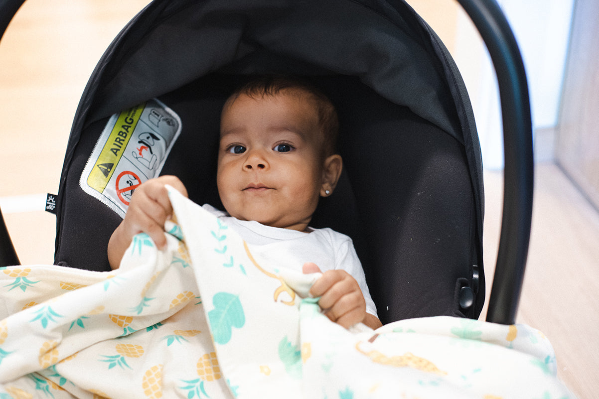 Baby sitzt in Auto-Kindersitz und greift nach der Windelbär Babydecke Design Dschungel.