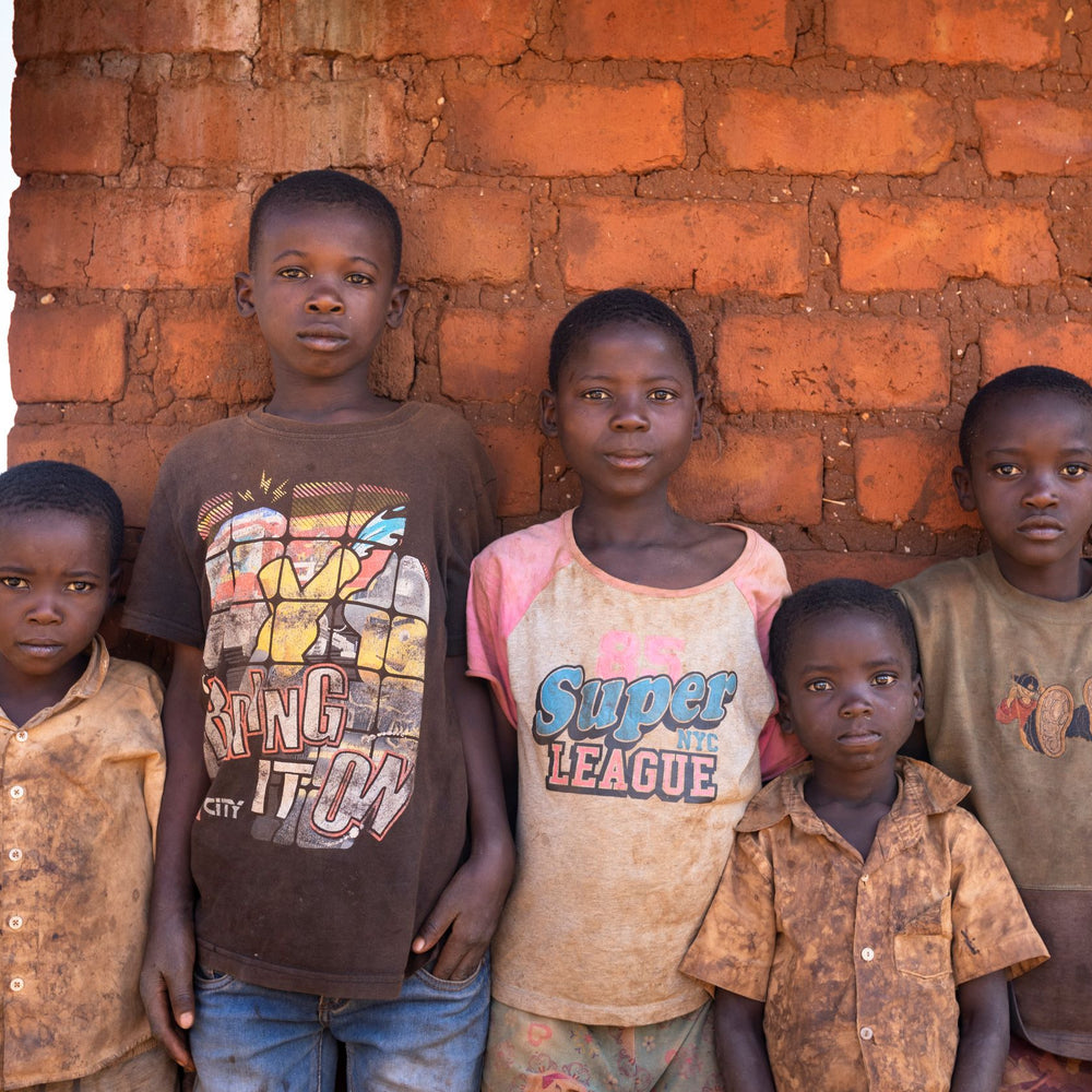 Fünf Kinder vor einer rohen Ziegelmauer.