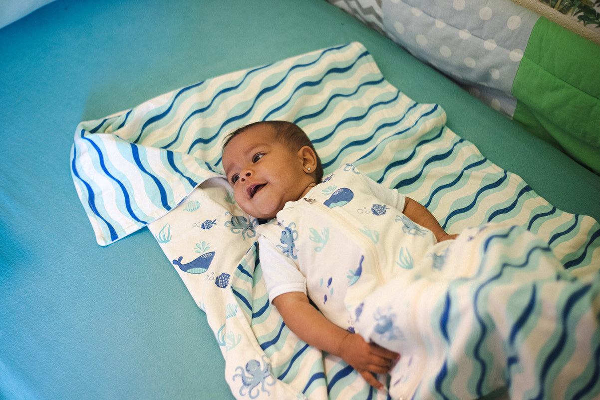 Baby liegt in einem Windelbär Schlafsack Design Meer auf einer Babydecke.